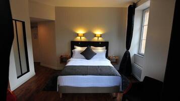 Una habitación de hotel ordenada con una cama grande, dos lámparas de noche, un ventanal con cortinas y suelo de madera.