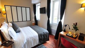 A hotel room with a bed, a desk with a chair, a TV, and a window with curtains.