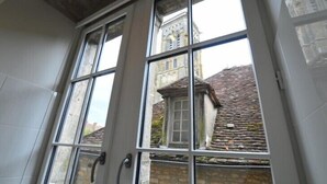 A room with a large window offering a view of a historic building with a stone facade and a tiled roof. - Hôtel & Restaurant SY La Terrasse (Vezelay)