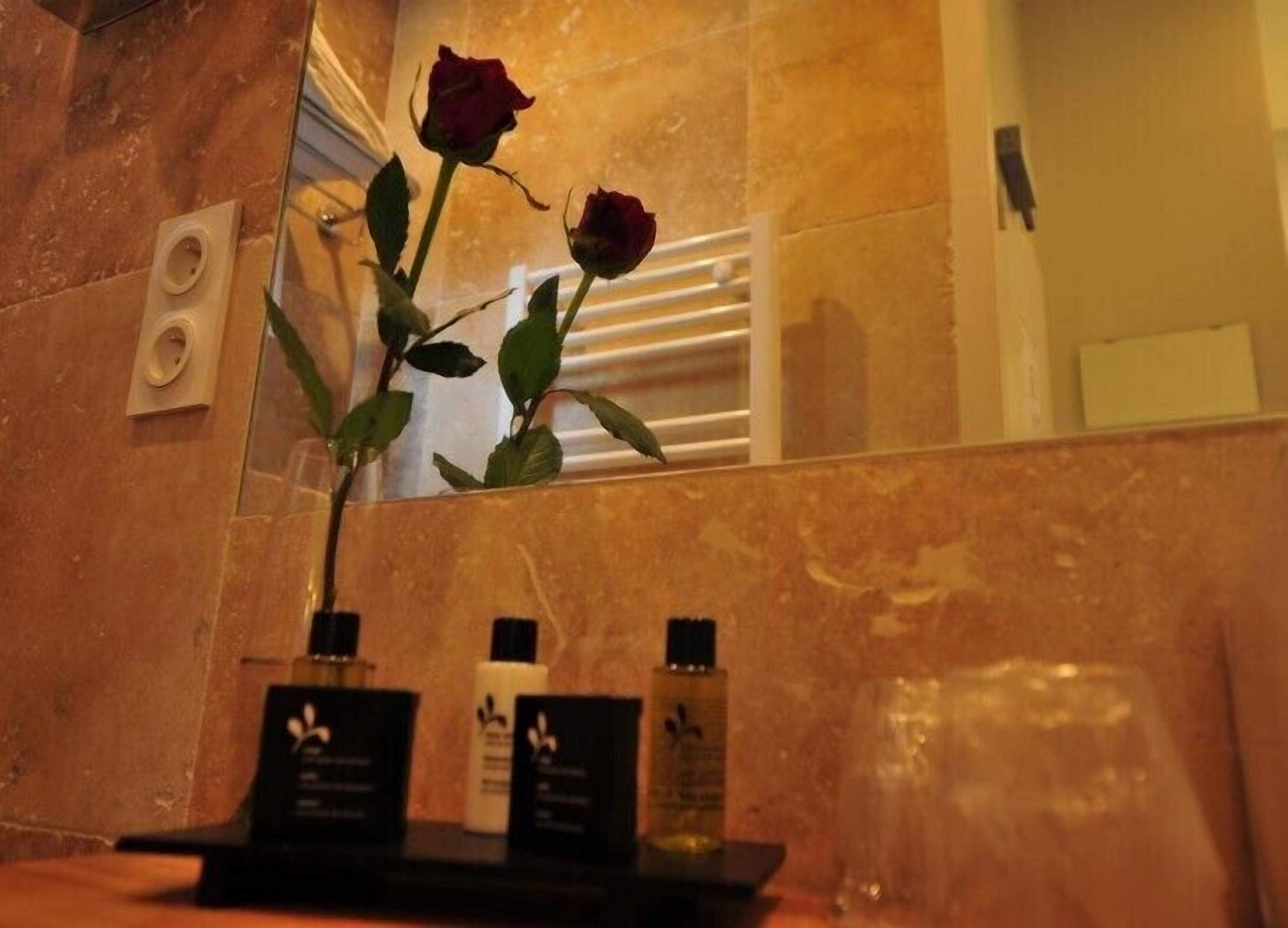 Un baño con pared de mármol, un espejo, una rosa y artículos de tocador en una bandeja.