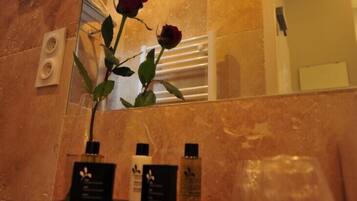 Un baño con pared de mármol, un espejo, una rosa y artículos de tocador en una bandeja.
