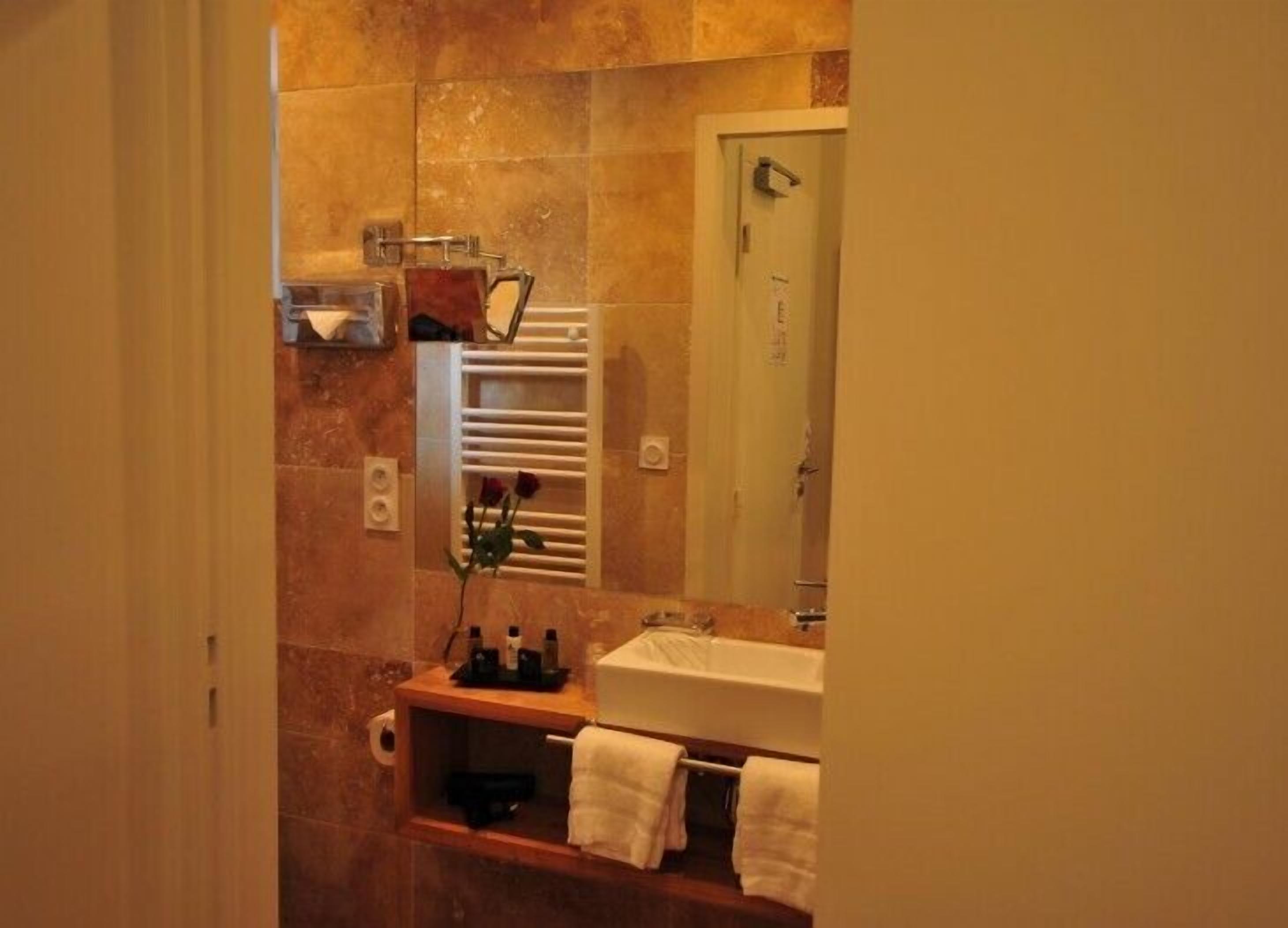 Une salle de bain avec un mur en marbre, un lavabo blanc, un porte-serviettes et un miroir.