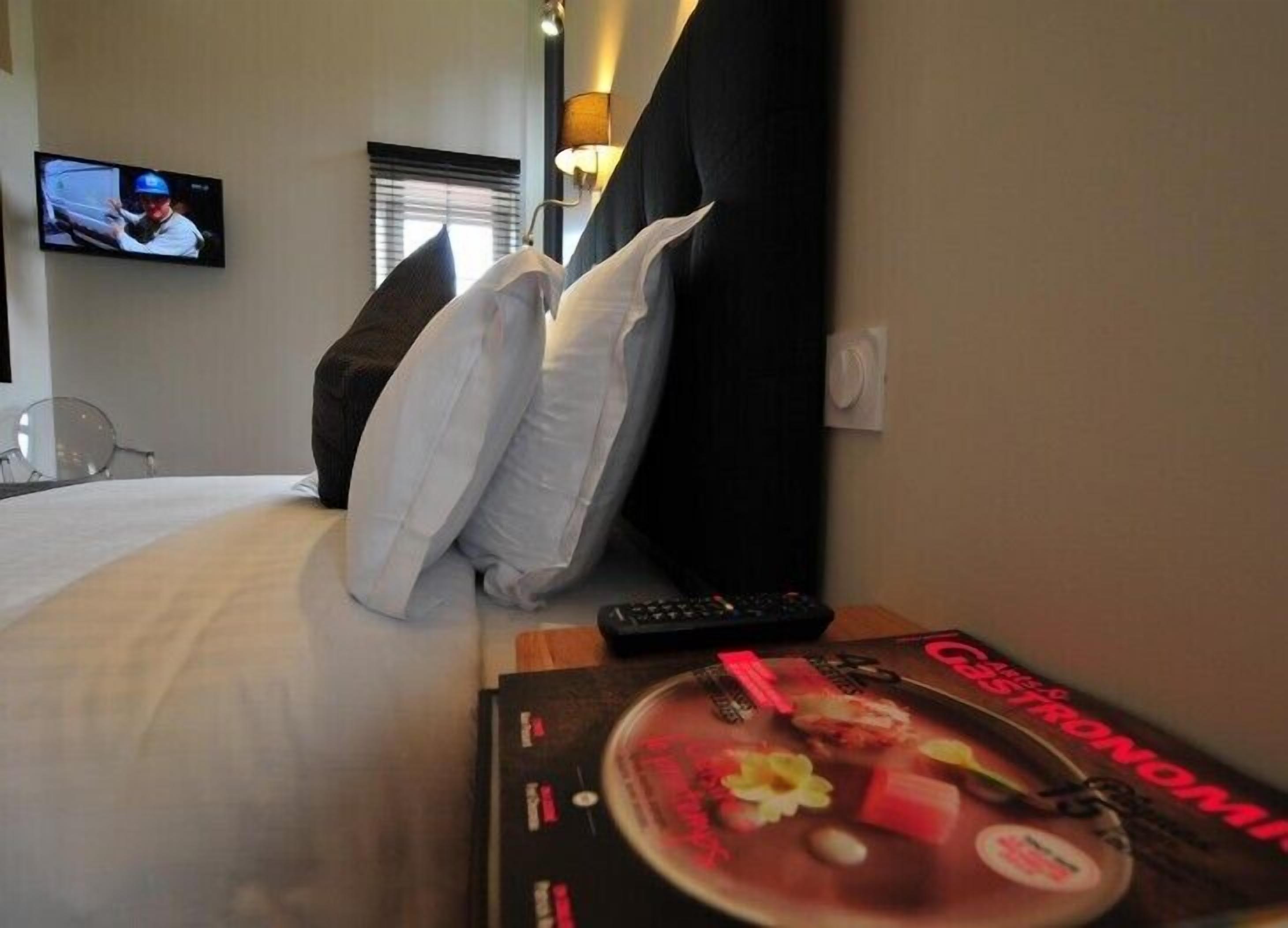 Una habitación de hotel con cama, almohadas, un control remoto y una revista sobre la mesita de noche.