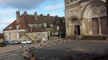 Un bâtiment historique à la façade en pierre, doté d’une grande entrée en arc de cercle et d’une cour intérieure avec des bancs et des plantes en pot.