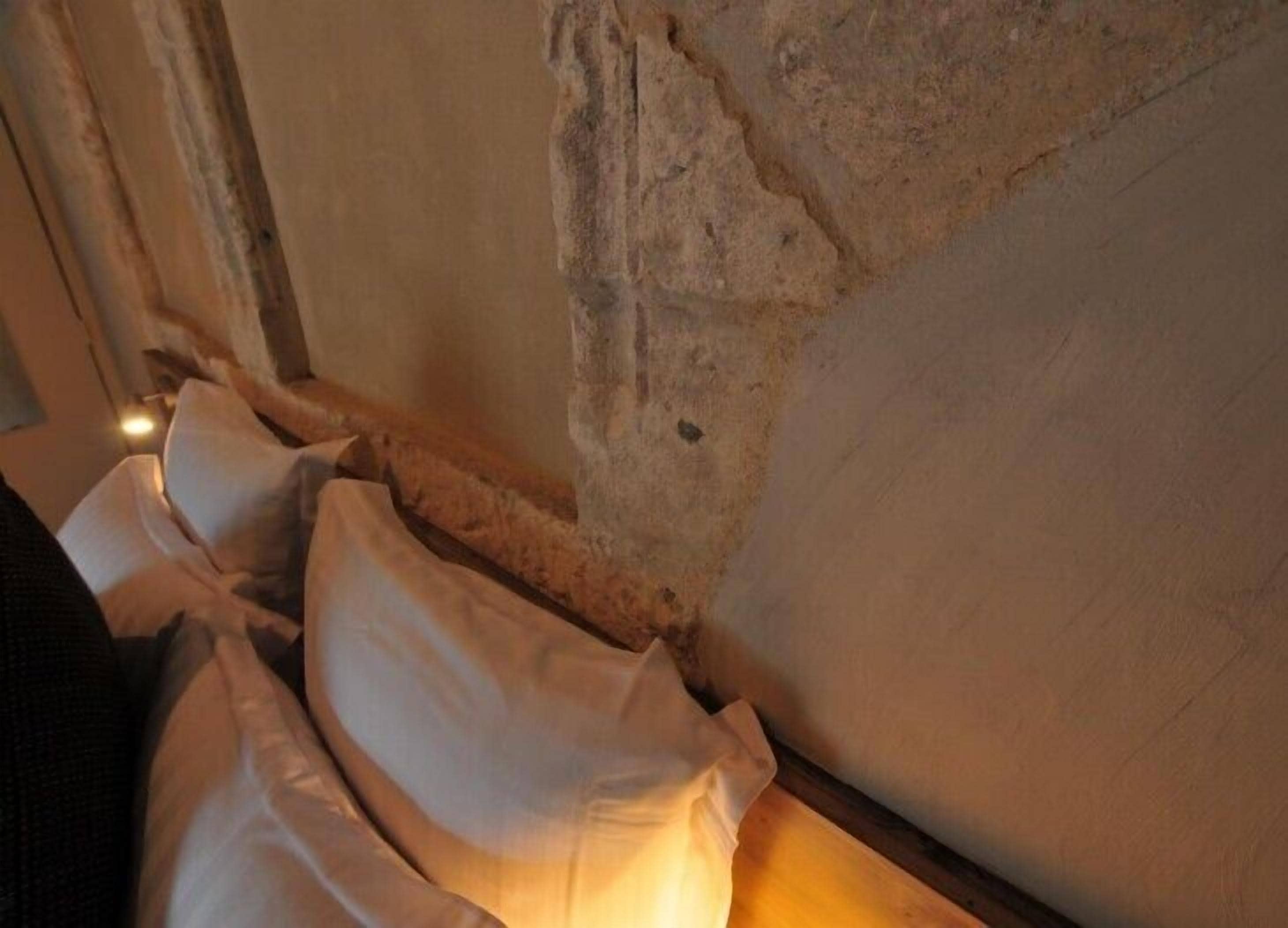 Quarto com parede de pedra e cama com roupa de cama branca.