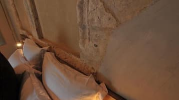 Quarto com parede de pedra e cama com roupa de cama branca.