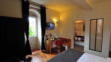A hotel room with a bed, a desk, a chair, a TV, and a bathroom visible through an archway.