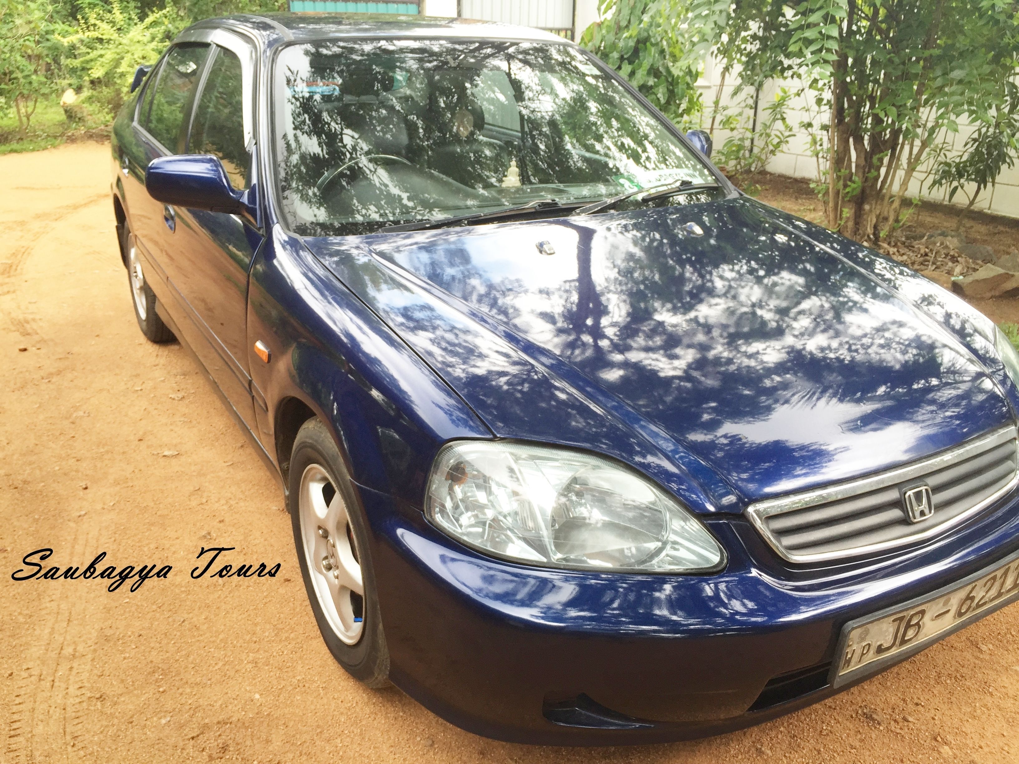 A blue car parked on a dirt road with trees in the background.