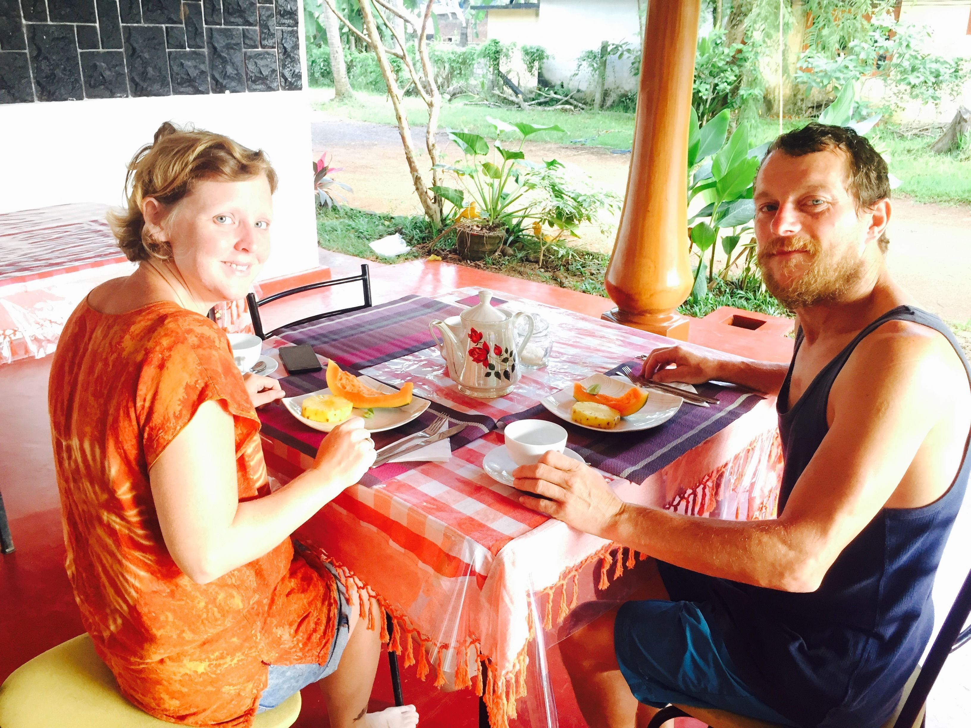 Dos personas sentadas en una mesa al aire libre con mantel a cuadros, platos de comida y un calentador de agua.