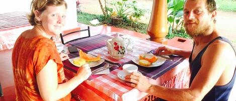 Two people seated at an outdoor table with a checkered tablecloth, plates of food, and a teapot.