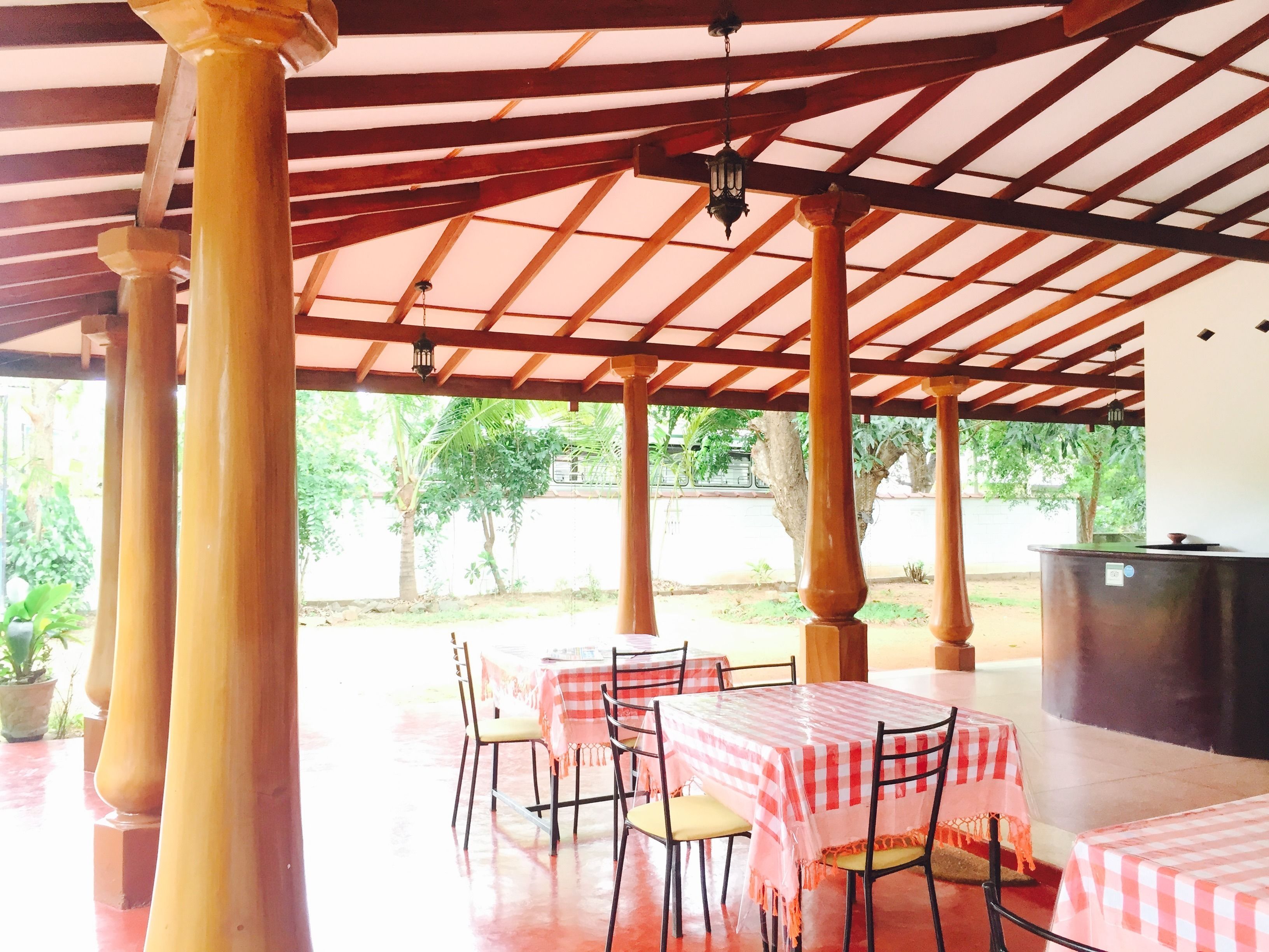 An outdoor covered patio with wooden columns, tables with checkered tablecloths, and hanging lanterns.