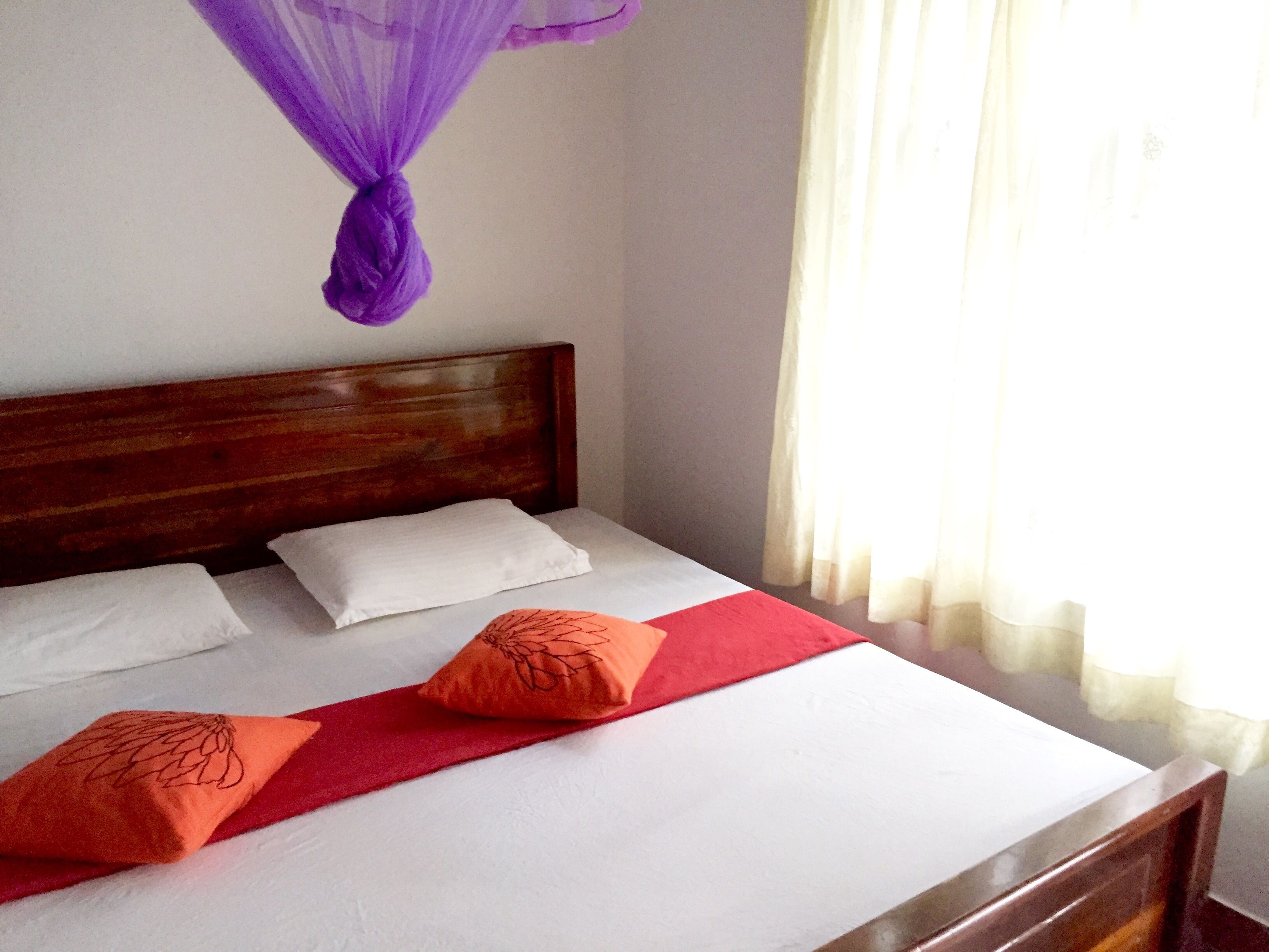 A bed with a wooden headboard, white bedding, and two orange pillows.