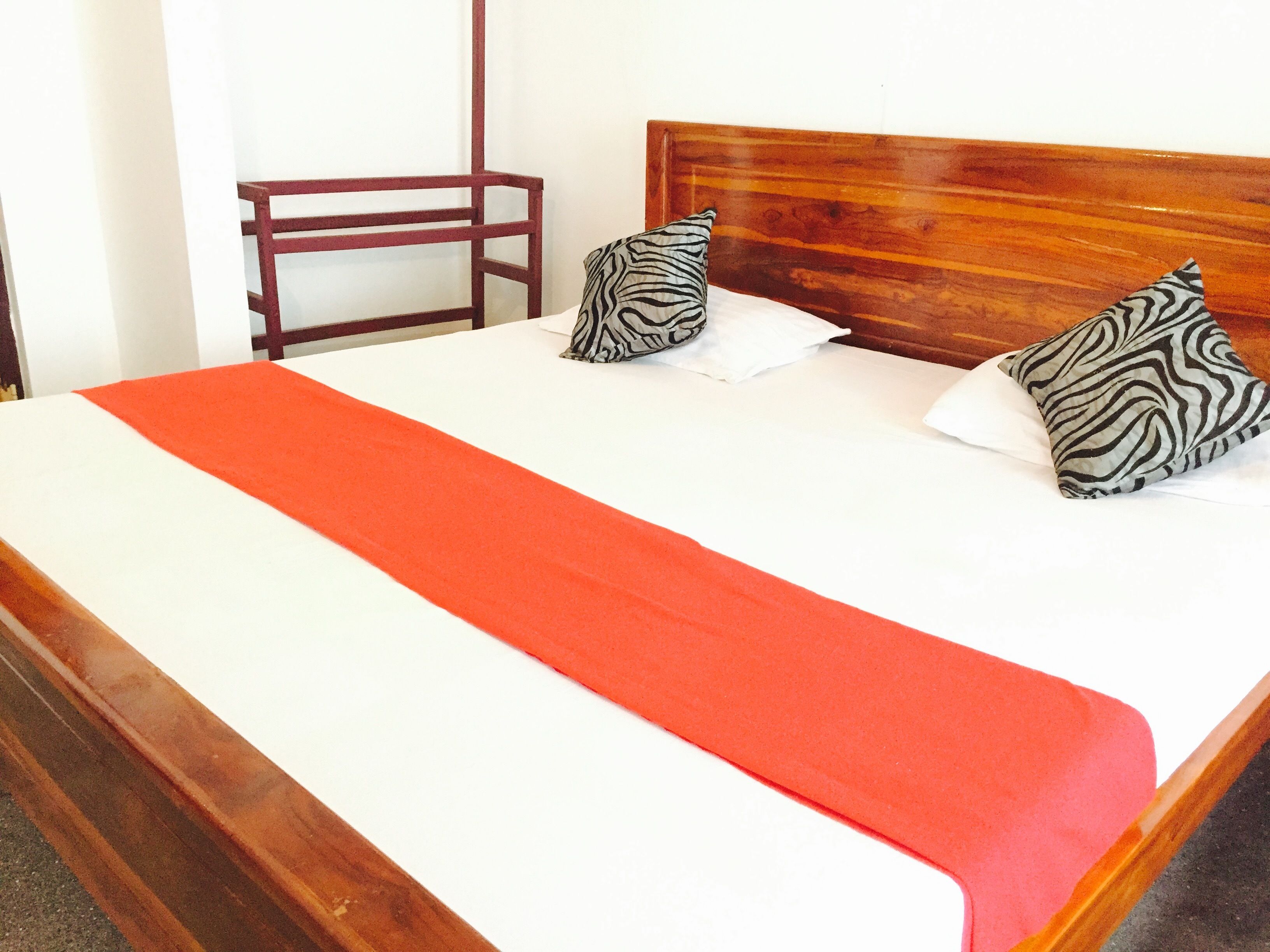 A bed with a wooden headboard, two zebra-patterned pillows, and a red bedspread.