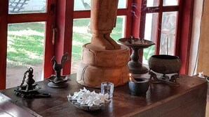 Une statue représentant une figure assise sur un piédestal, placée sur une table en bois, avec une fenêtre en arrière-plan.