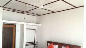 Une chambre d’hôtel avec un lit, une tête de lit en bois et un ventilateur de plafond.