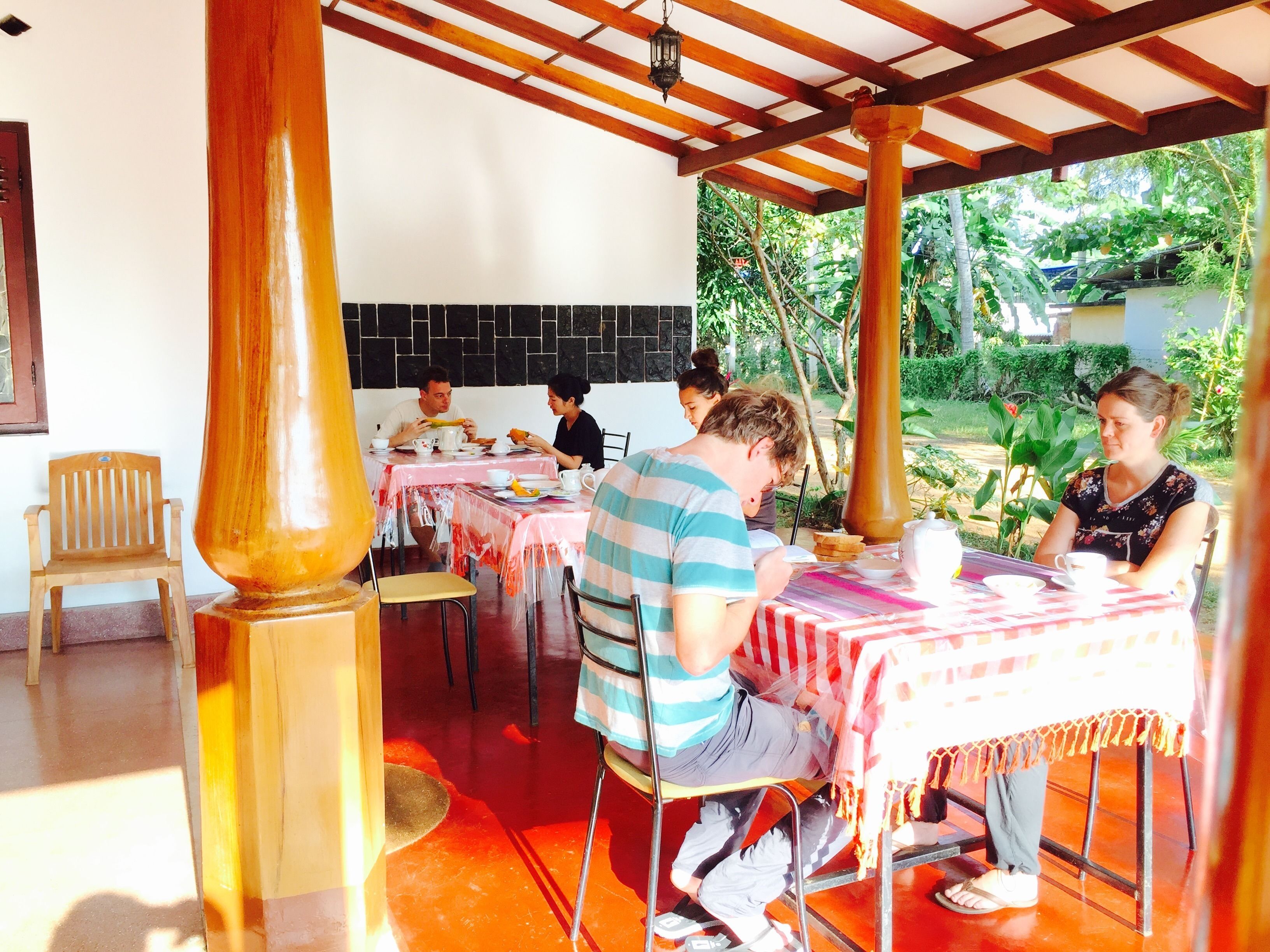 Un comedor con mesas cubiertas de plástico, sillas de madera y una pared de azulejos.