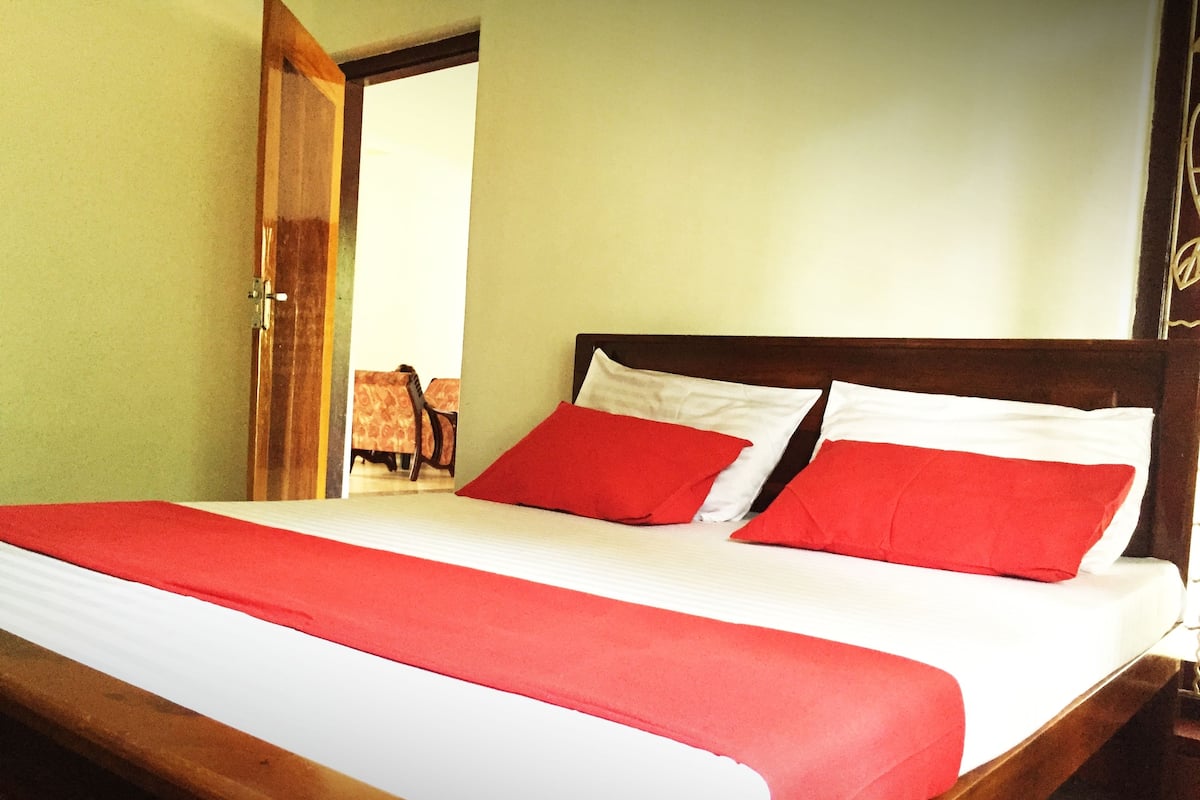 Uma cama com estrutura de madeira, roupa de cama branca e almofadas vermelhas.