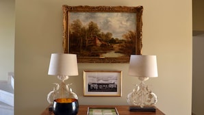 Een houten tafel met twee lampen, een schaal en ingelijste foto's aan een muur.