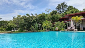 Una piscina azul cristalina rodeada de exuberante vegetación y un edificio con techo rojo.