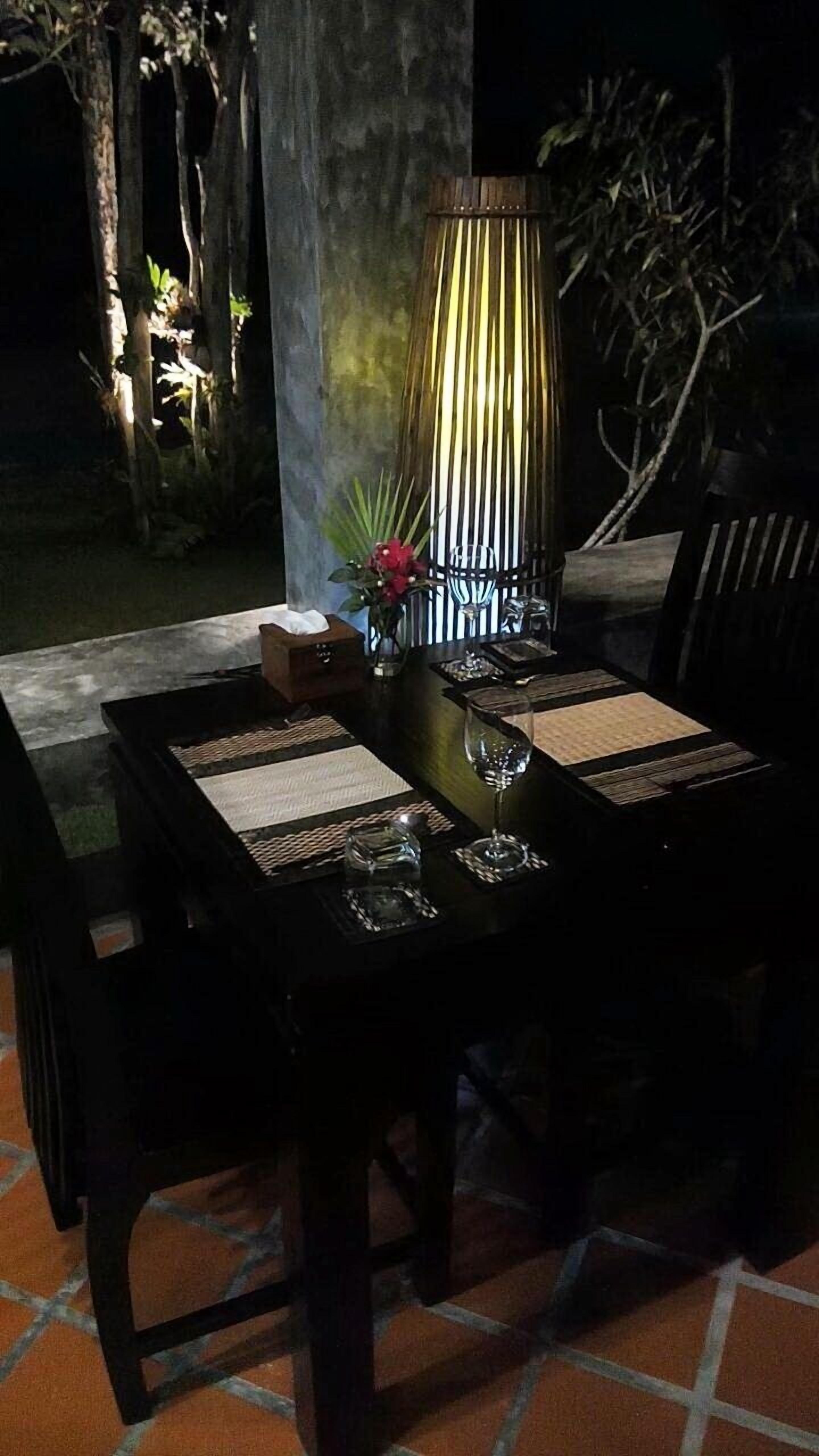 A dining table set for two with a candle centerpiece, a vase with flowers, and a bottle of water.