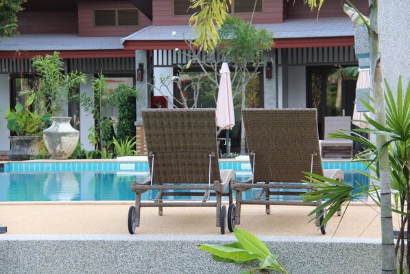 A poolside area with two wicker lounge chairs and a small table, surrounded by potted plants and a building in the background. - Arthaya Villas (Ko Lanta)