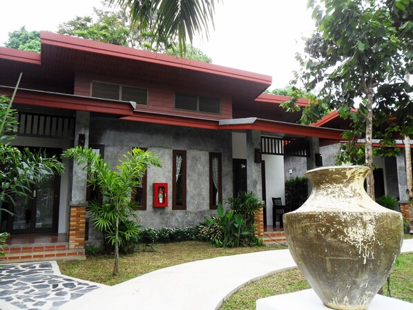A building with a red roof and grey walls, surrounded by greenery and a large decorative vase. - Arthaya Villas (Ko Lanta)