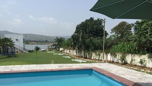 A swimming pool with a view of a grassy area, a small building, and a body of water in the distance. - Volta Escape Resort (Atimpoku)