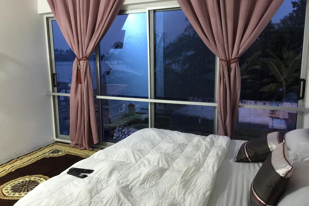 A bedroom with a large window, a bed with white bedding, and a remote control on the bed.