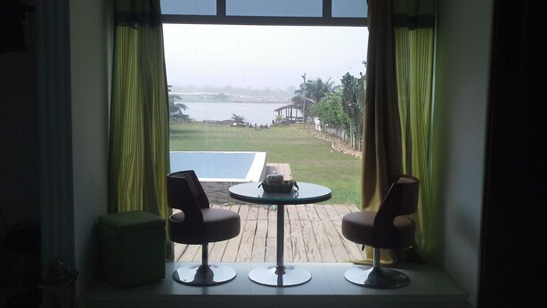 A room with a view of a lake, two chairs, a small table, and a green ottoman. - Volta Escape Resort (Atimpoku)