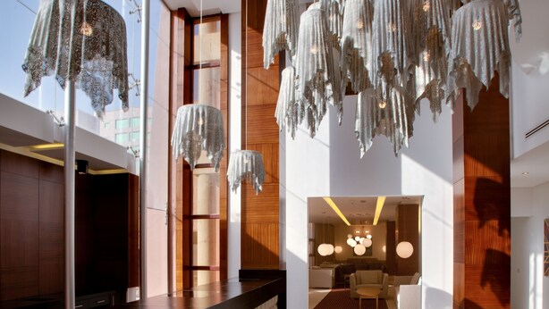 Un hall d’hôtel moderne avec un comptoir d’accueil central, des luminaires suspendus et une vue sur la salle à manger.