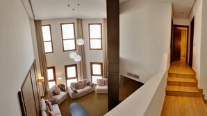 Un vaste espace de vie doté d’un haut plafond, de grandes fenêtres et d’un escalier en bois.
