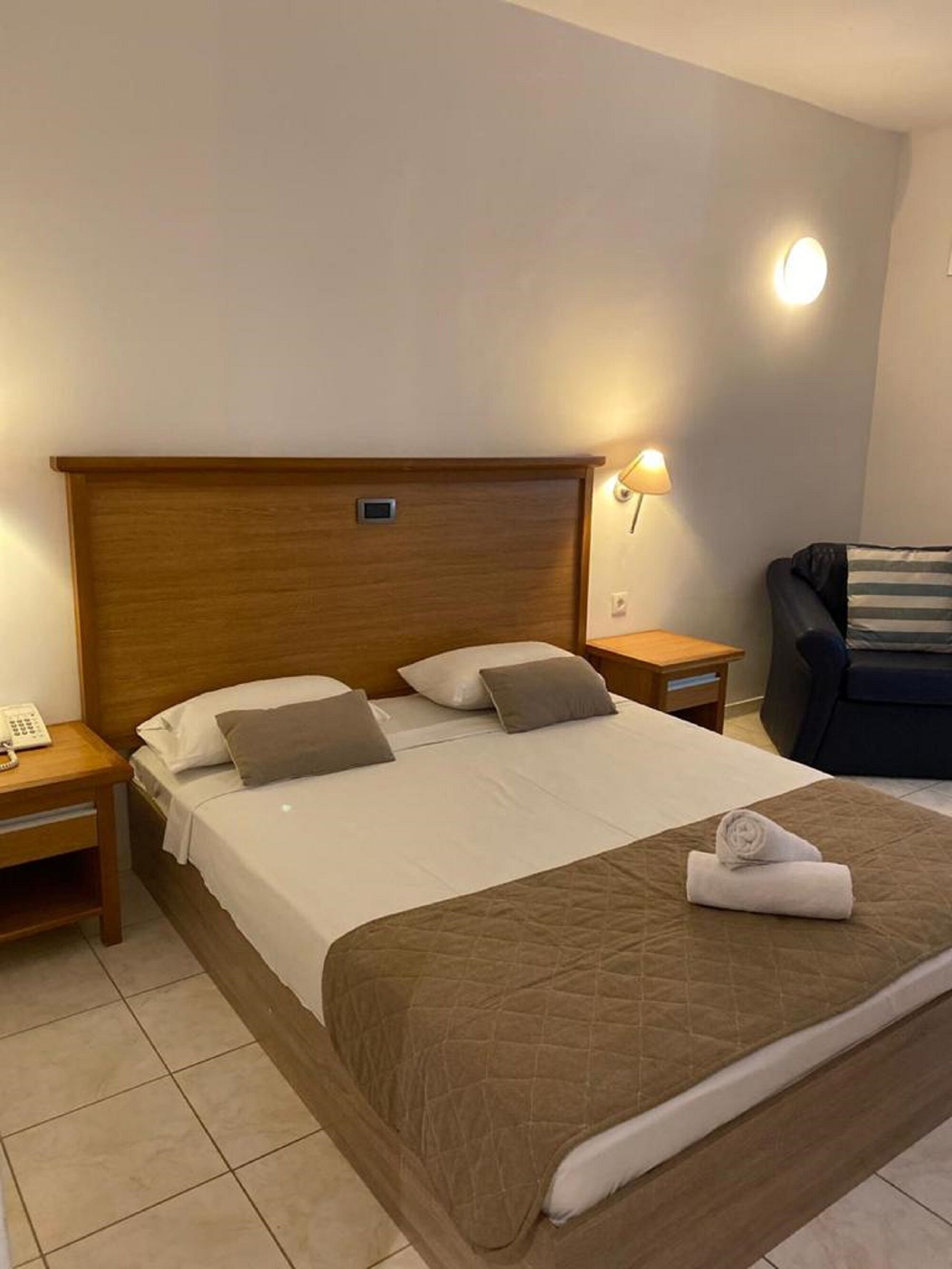 A neatly made bed with a wooden headboard, a bedside lamp, and a telephone on a wooden nightstand.