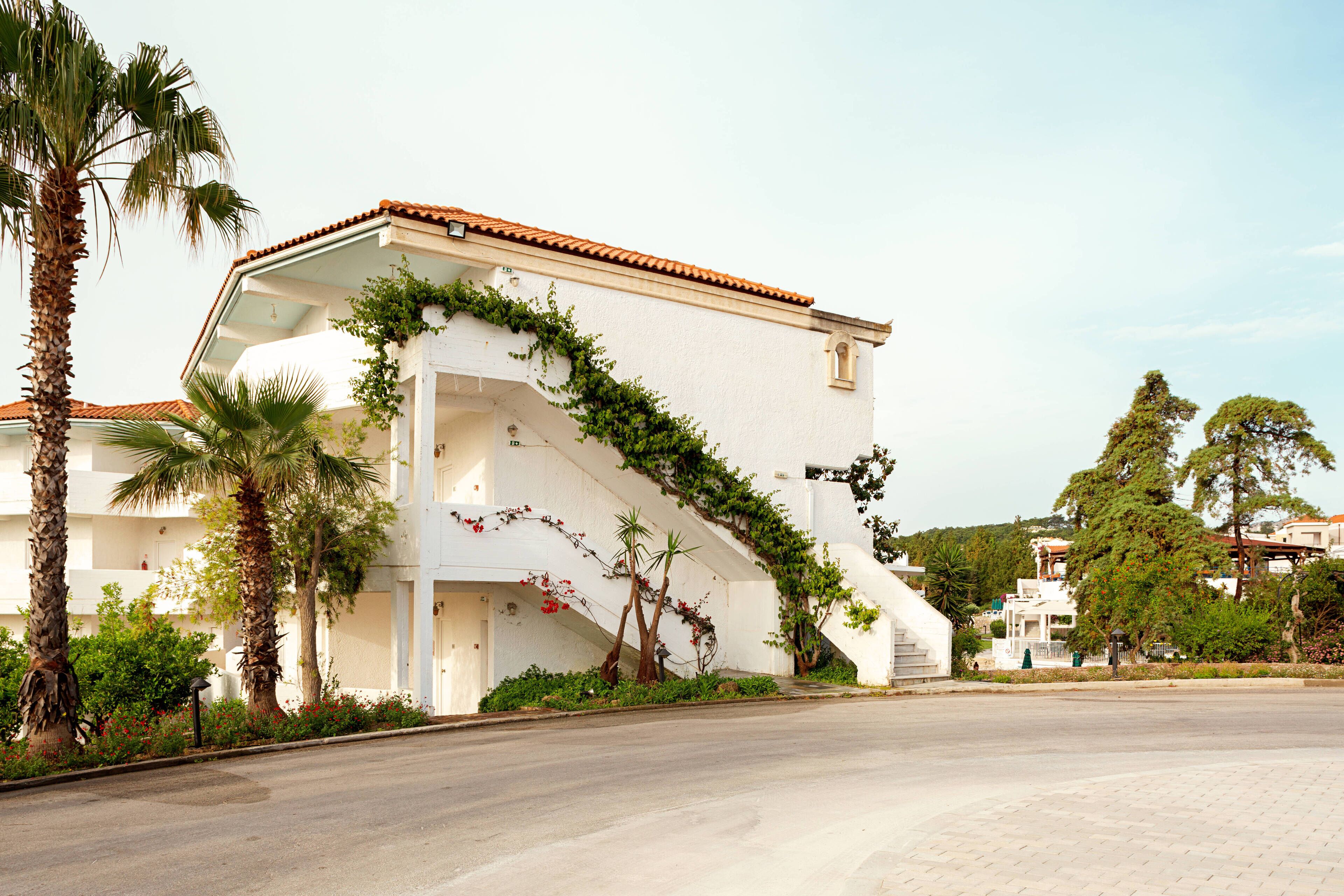 Un bâtiment blanc surmonté d’un toit recouvert de tuiles rouges, entouré de palmiers et de verdure.