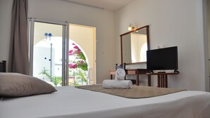 A hotel room with a bed, a television, a mirror, and a view of a balcony with flowers. - Cyprotel Faliraki - All Inclusive (Rhodes)