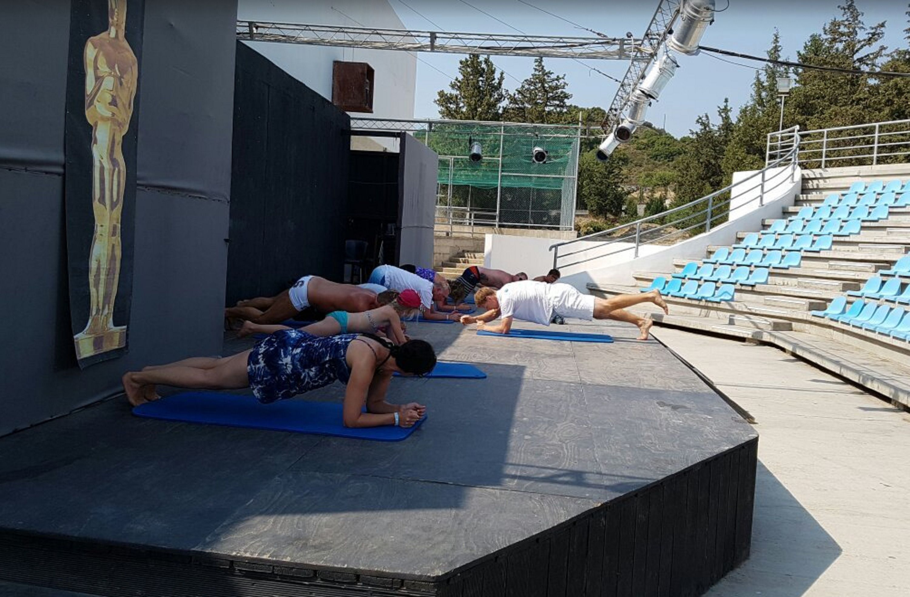 Un grupo de personas practicando yoga sobre esterillas azules al aire libre.