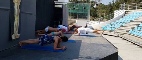 Un grupo de personas practicando yoga sobre esterillas azules al aire libre.