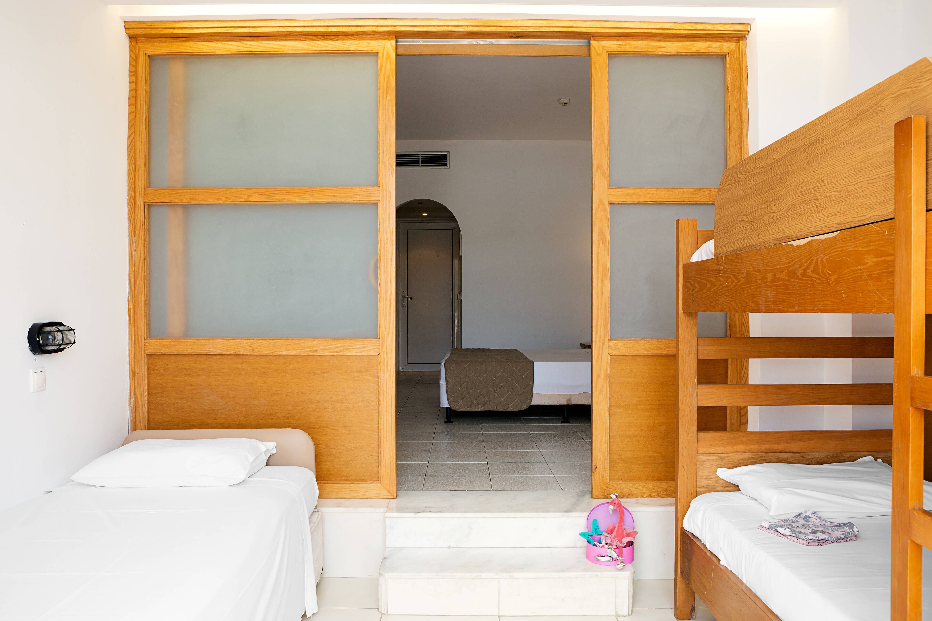 Habitación de hotel con una cama litera de madera, una cama individual y un baño visible a través de una puerta abierta.