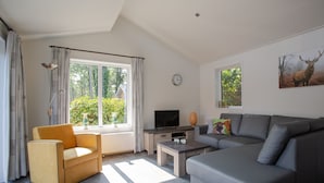 A modern living room with a sofa, armchair, and a television on a wooden stand. - De Thijmse Berg (Rhenen)