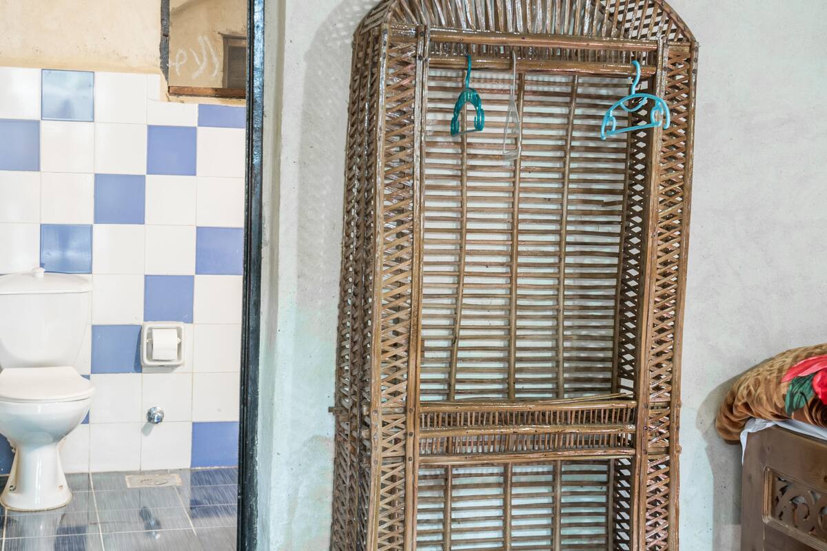 A bathroom with a white toilet, blue and white checkered tiles, a wicker shower enclosure, and a small shelf with a white container.
