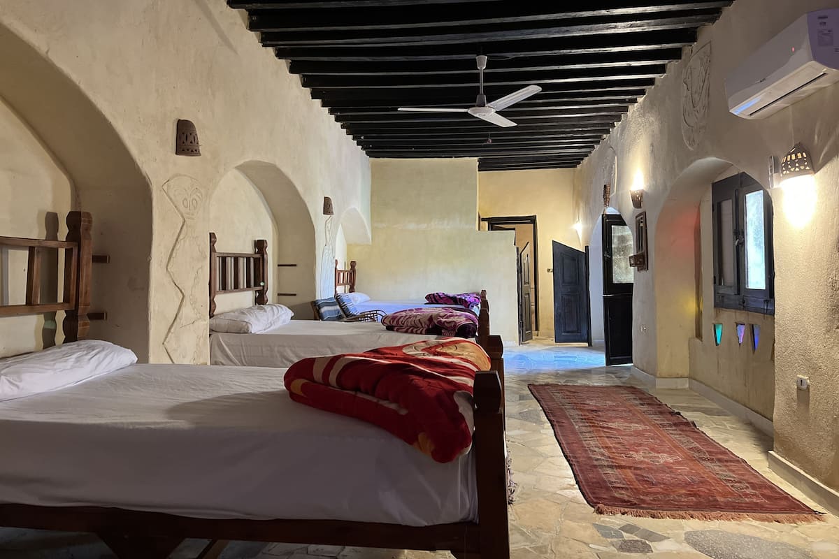 A hotel corridor with two beds, a ceiling fan, an air conditioning unit, and a patterned rug.