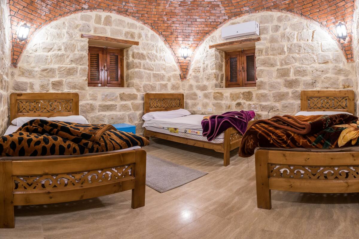 A room with two wooden beds, stone walls, and a tiled floor.