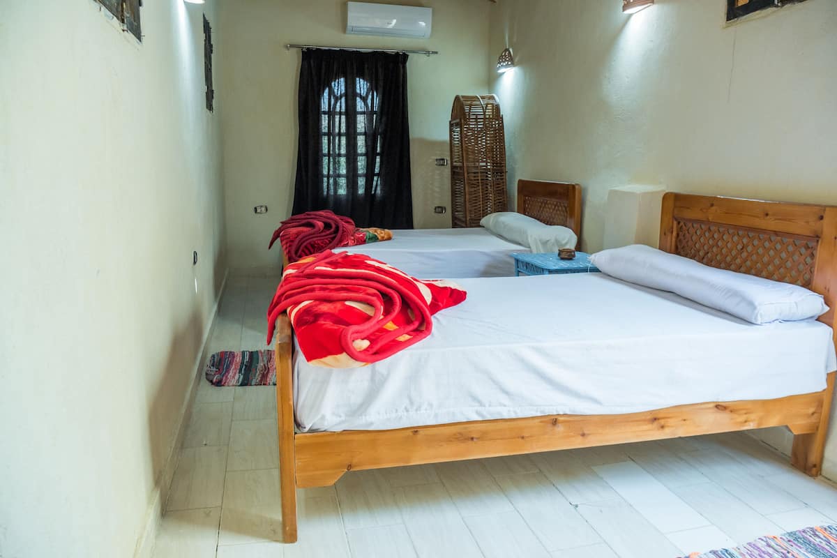 A room with two wooden beds, white bedding, a black curtain, and a woven basket.