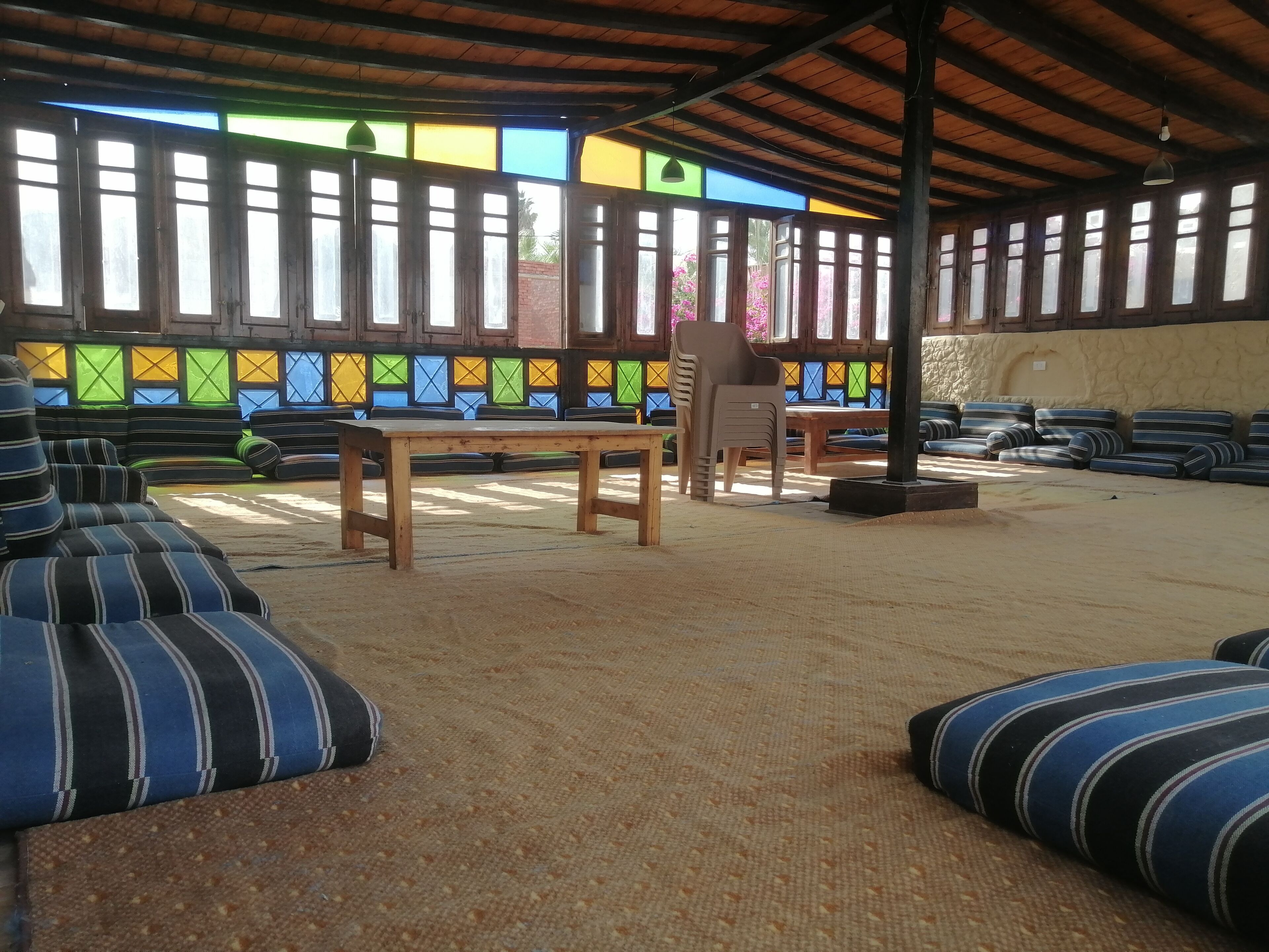 Un área de estar al aire libre con techo, cojines a rayas, una mesa de madera y una silla.