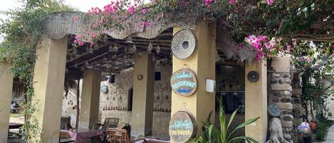 Un área de estar al aire libre rústica con un pérgola, pilares de piedra y un letrero que indica un restaurante.