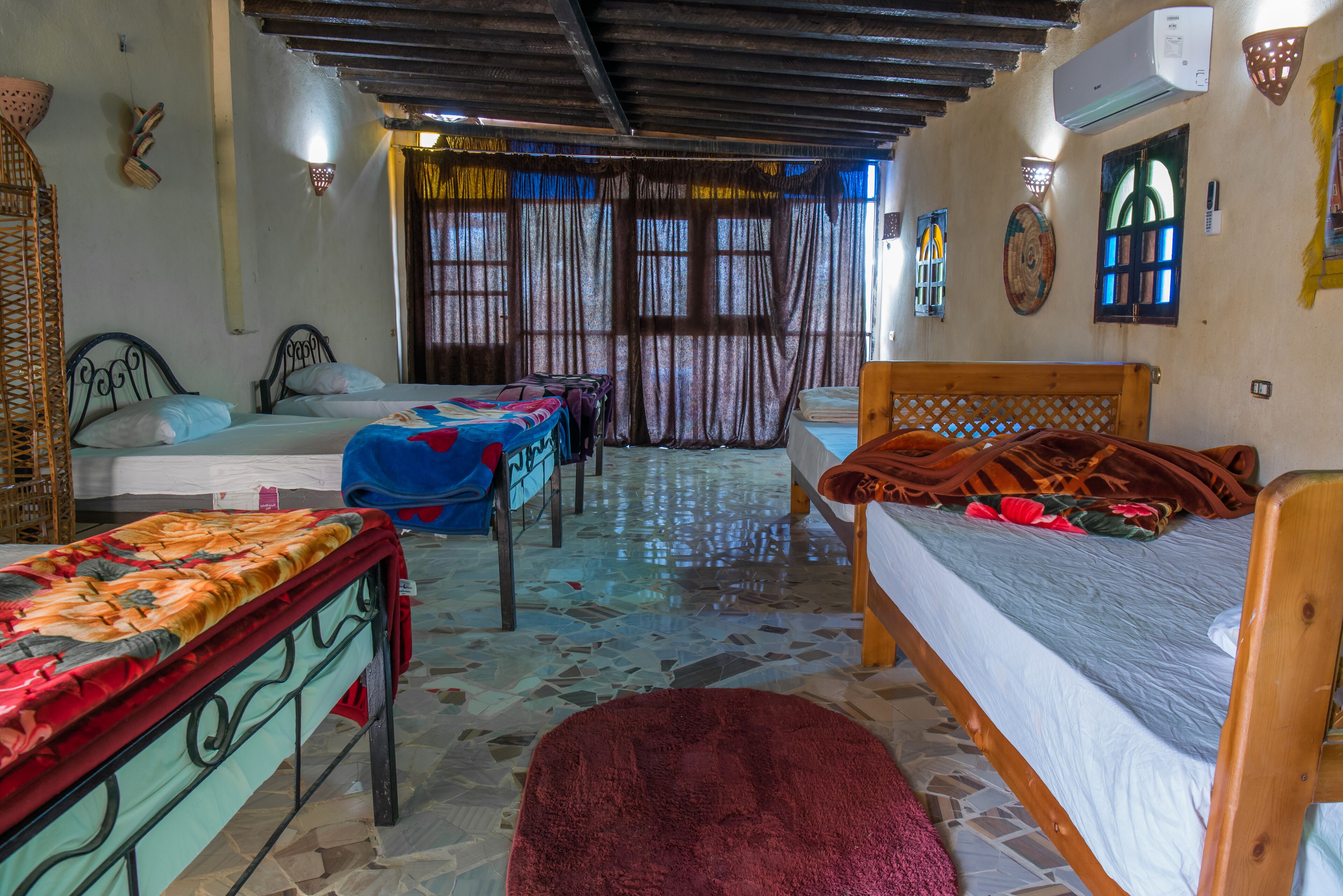 A room with three beds, a wooden ceiling, and a tiled floor.