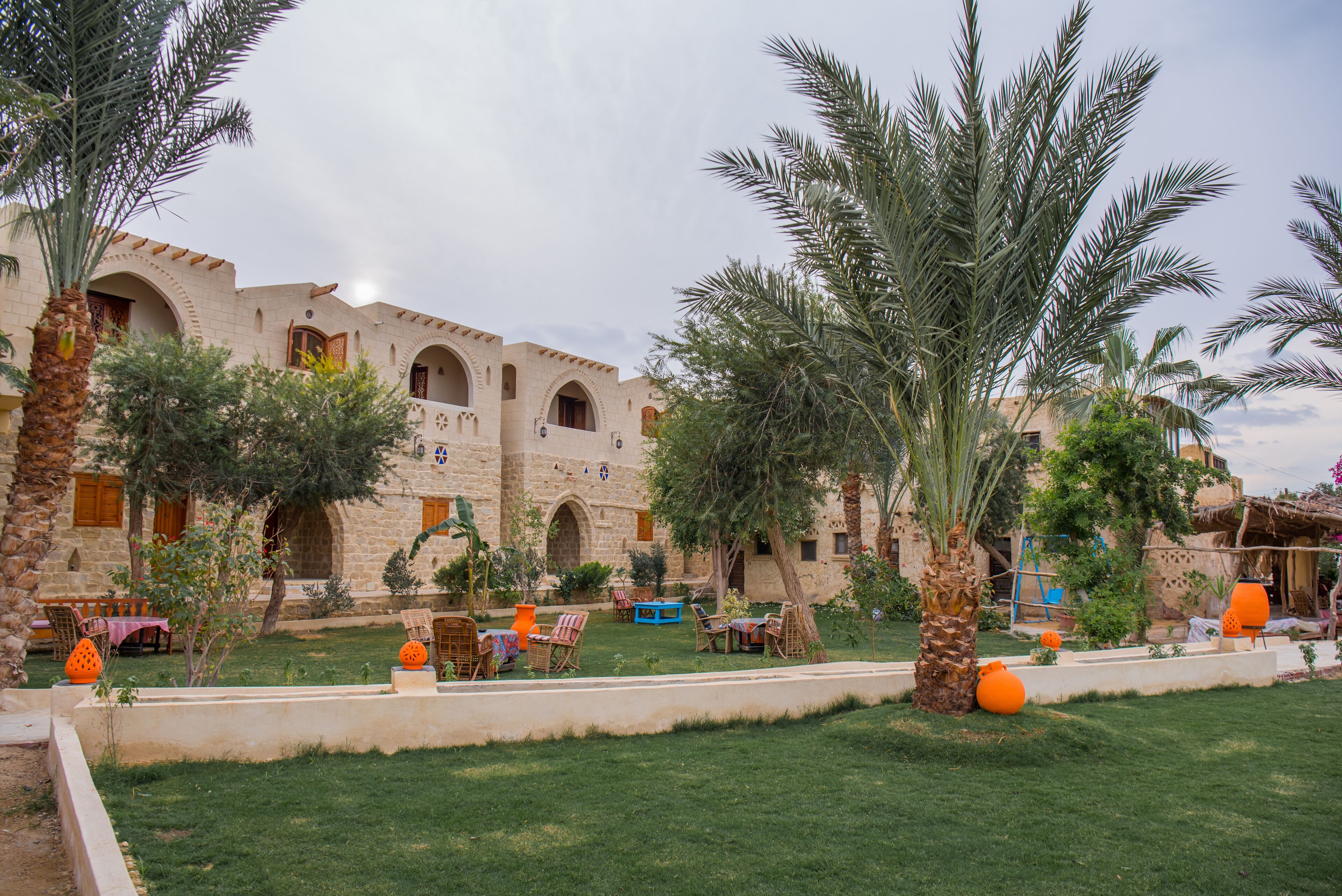 A courtyard with a stone building, palm trees, and outdoor seating.