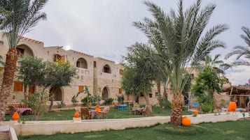 A courtyard with a stone building, palm trees, and outdoor seating.