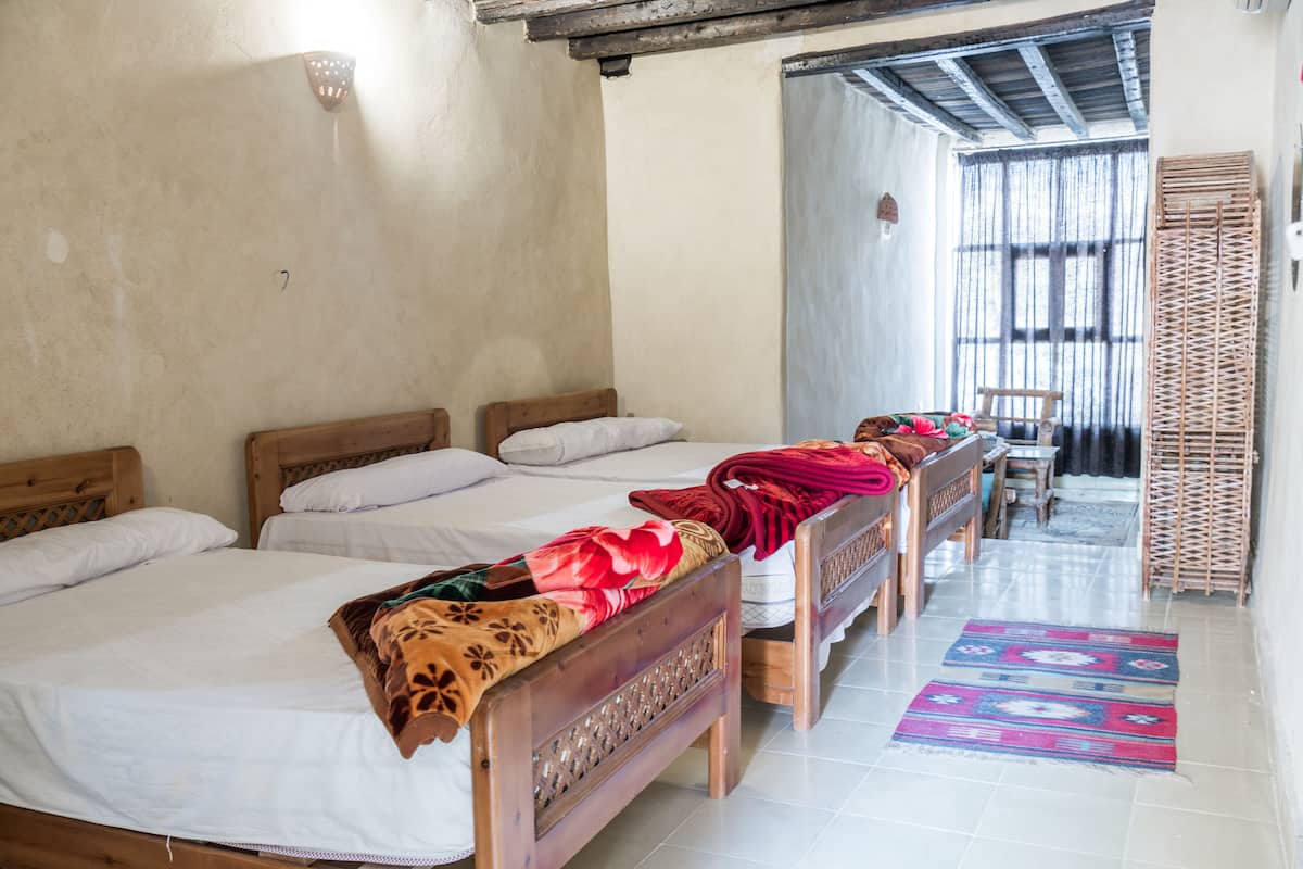 A room with four wooden beds arranged in a row, a wooden table, and a patterned rug on the floor.