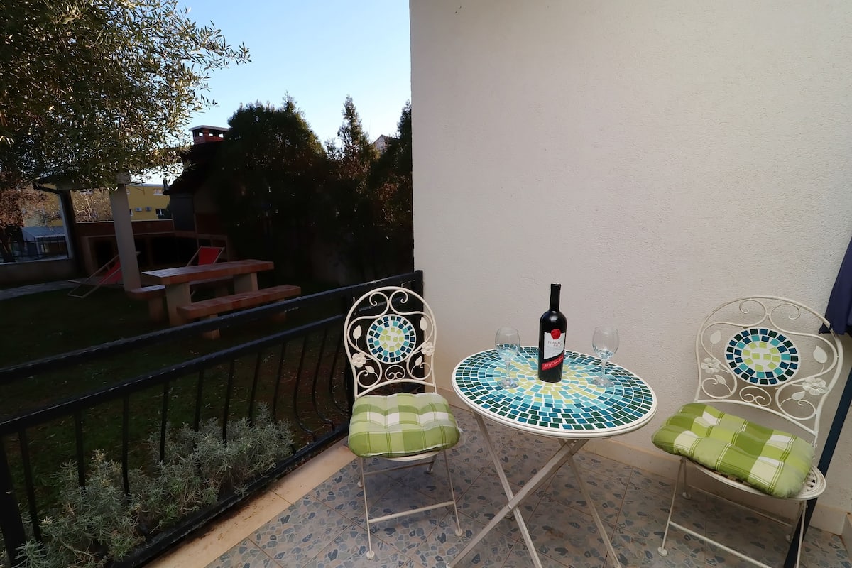 A balcony with two metal chairs and a table, a bottle of wine, and a glass on the table.