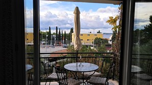 A balcony with a round table and chairs, an umbrella, and a view of a parking lot and buildings. - Apartments Trstenica (Orebic)